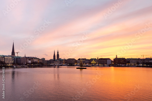 Sunset in Hamburg. Panoramic view of the decorated city center from Alster Lake, view to Hamburg Rathaus and a christmas tree installed in the center of the lake. Atmosphere before the New Year.