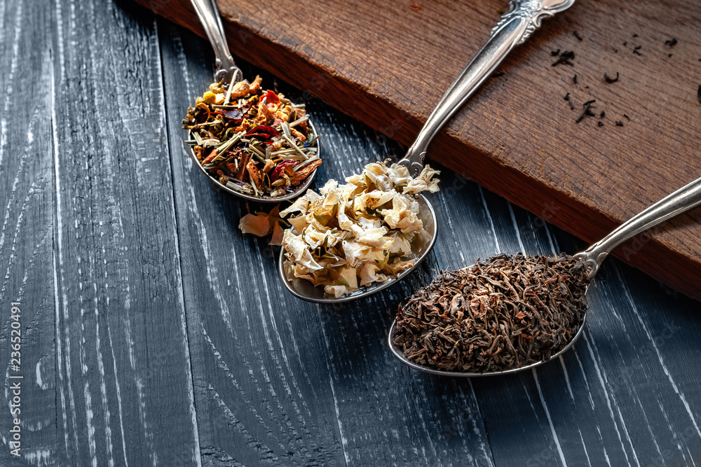 Fototapeta premium Various types of dry tea leaves and jasmine. The composition of tea with different types of tea from different herbs. Tea leaves and jasmine flowers on wooden background.