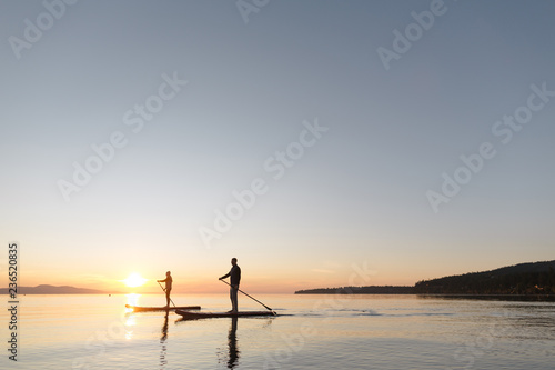 Couple stand up paddle boarding together at sunrise