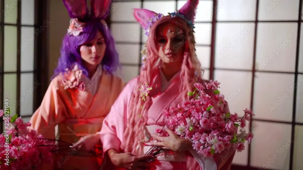 Two beautiful anime girls with pink and purple wigs wearing pink and holding sakura branches. Two beautiful anime girls with pink and purple wigs wearing pink and holding sakura branches.