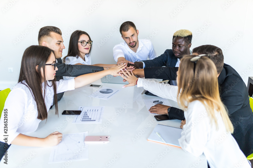 Together we are stronge. Group of happy business people holding hands together while sitting around the desk Together we are stronge. Group of happy business people holding hands together while sitting around the desk