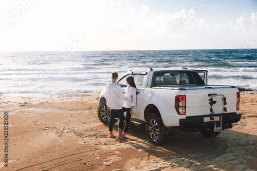 A young couple with a pick up truck on a deserted beach.young couple by pick-up truck parked on beach
