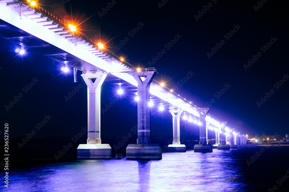 Beautiful view of the bridge illuminated by neon shimmering light at night. Bridge stands on the river. Long exposure. Night scene. Close-up
