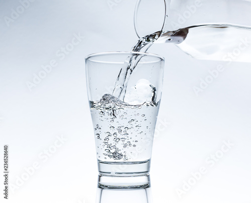 Pouring water into glass from a jar isolated on white background