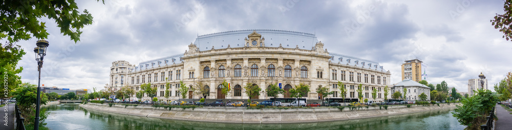 Panoramic view of Palace of Justice in downtown Bucharest reflected in Dambovita River; dramatic cloudy sky in the background, Bucharest, Romania