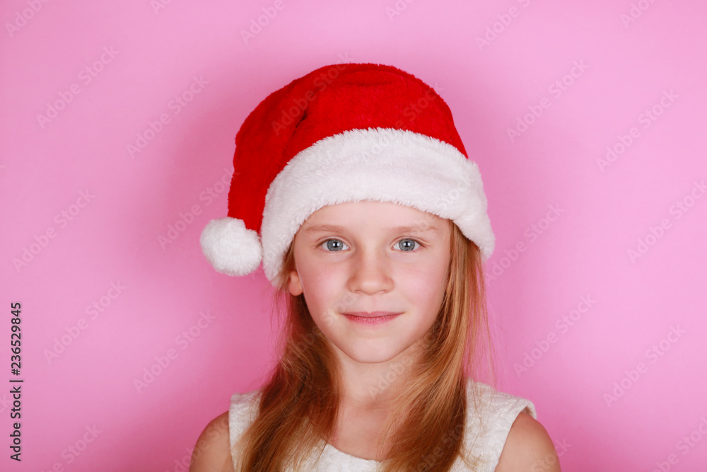 Happy smiling girl in Santa cap and white dress on a pink background, copy space. Happy smiling girl in Santa cap and white dress on a pink background, copy space.