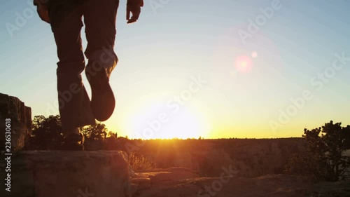 Grand Canyon National Park Silhouette of lone Caucasian female with backpack standing on the rocky edge sun flare sunset USA 