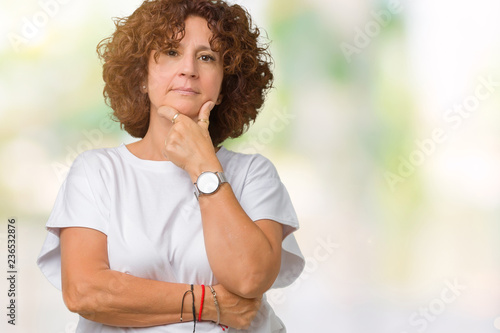 Beautiful middle ager senior woman wearing white t-shirt over isolated background looking confident at the camera with smile with crossed arms and hand raised on chin. Thinking positive.