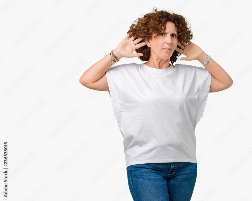 Beautiful middle ager senior woman wearing white t-shirt over isolated background smiling with hand over ear listening an hearing to rumor or gossip. Deafness concept. Beautiful middle ager senior woman wearing white t-shirt over isolated background smiling with hand over ear listening an hearing to rumor or gossip. Deafness concept.