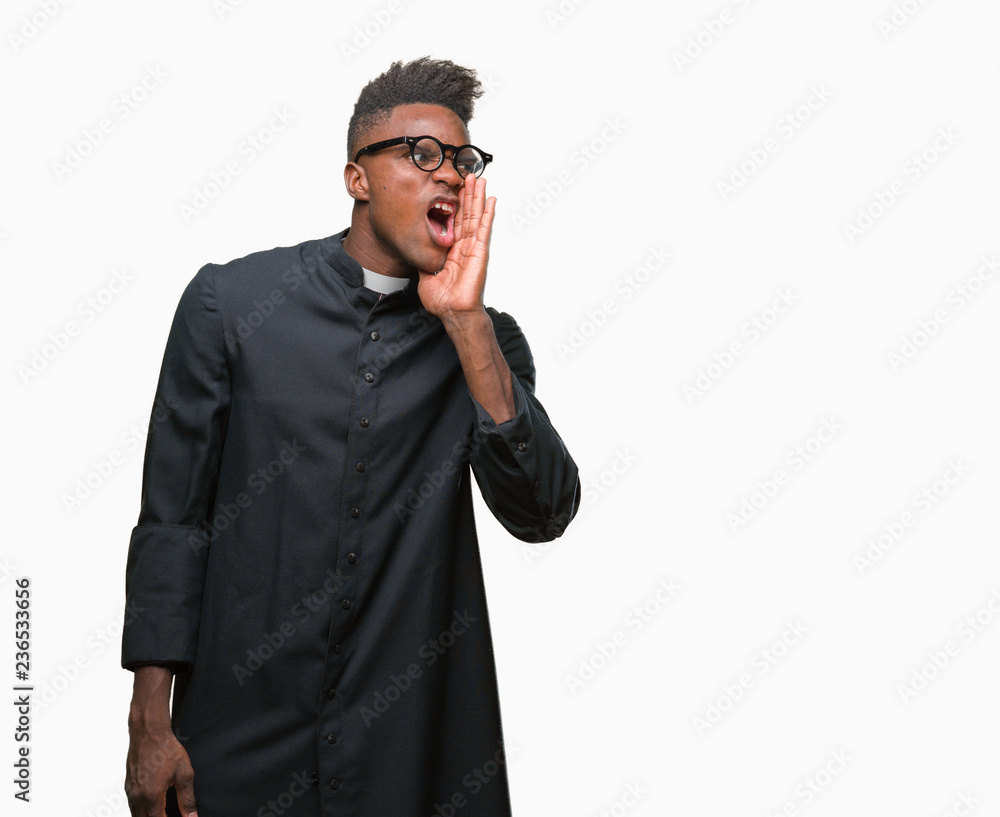Young african american priest man over isolated background shouting and screaming loud to side with hand on mouth. Communication concept. Young african american priest man over isolated background shouting and screaming loud to side with hand on mouth. Communication concept.