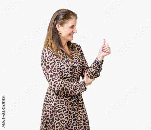 Beautiful middle age mature rich woman wearing leopard dress over isolated background Looking proud, smiling doing thumbs up gesture to the side