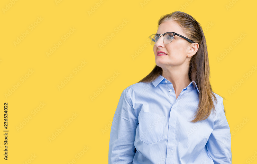 Beautiful middle age mature business woman wearing glasses over isolated background looking away to side with smile on face, natural expression. Laughing confident.