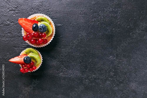 Fresh homemade fruit tart with strawberries, kiwi, blueberry, on dark stone background. Top view scene. Side border with copy space.