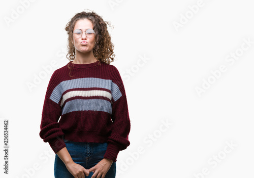 Beautiful brunette curly hair young girl wearing glasses over isolated background puffing cheeks with funny face. Mouth inflated with air, crazy expression.