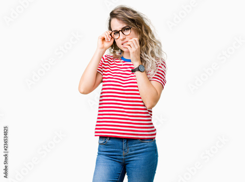 Beautiful young blonde woman wearing glasses over isolated background looking stressed and nervous with hands on mouth biting nails. Anxiety problem.