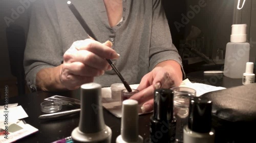 A nail technician applies polymer powder to her own nails as she repairs acrylic nails photo