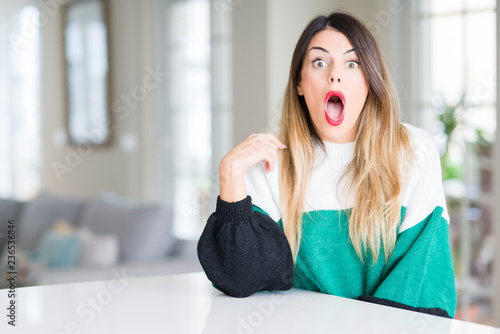 Free Download Young beautiful woman wearing winter sweater at home In shock face, looking skeptical and sarcastic, surprised with open mouth - GFXLoad