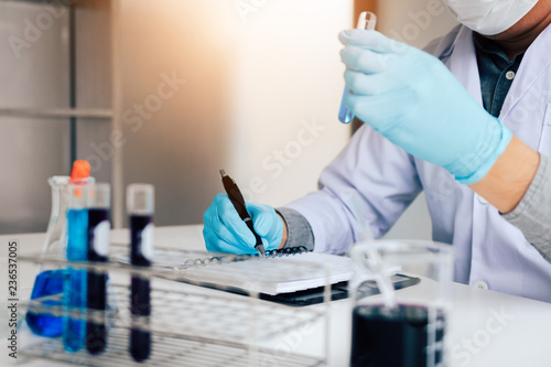Scientist recording making note on book with his findings test tube in lab.