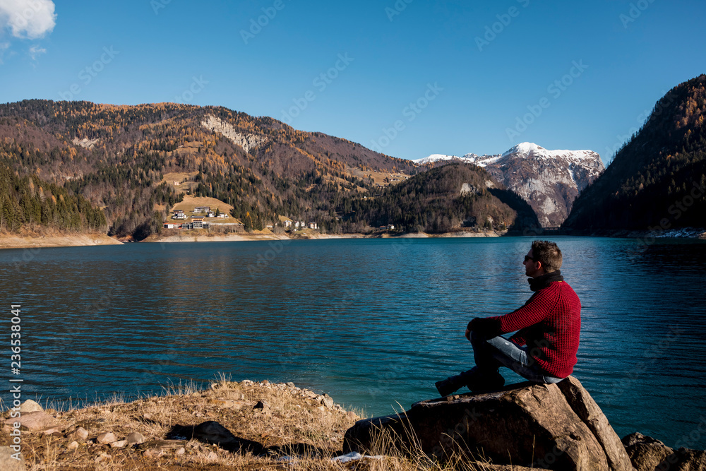 Man walking down a cliff along a lake on mountains