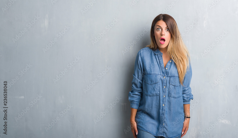 Young adult woman over grunge grey wall wearing denim outfit afraid and shocked with surprise expression, fear and excited face. Young adult woman over grunge grey wall wearing denim outfit afraid and shocked with surprise expression, fear and excited face.