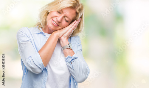 Middle age blonde woman over isolated background sleeping tired dreaming and posing with hands together while smiling with closed eyes.