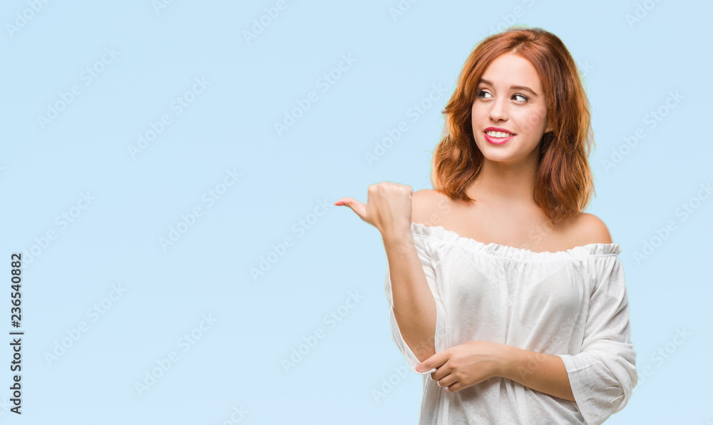 Young beautiful woman over isolated background smiling with happy face looking and pointing to the side with thumb up. Young beautiful woman over isolated background smiling with happy face looking and pointing to the side with thumb up.
