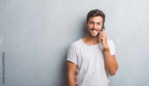 Handsome young man over grey grunge wall speaking on the phone with a happy face standing and smiling with a confident smile showing teeth © Krakenimages.com