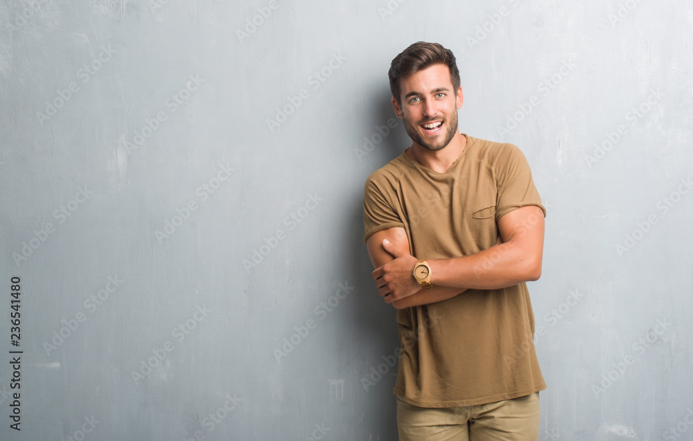 Handsome young man over grey grunge wall happy face smiling with crossed arms looking at the camera. Positive person.