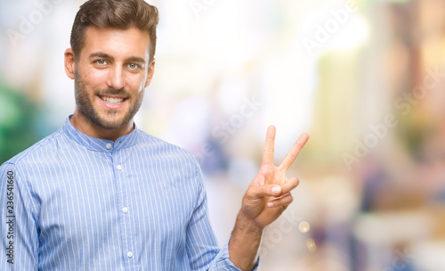Young handsome man over isolated background smiling with happy face winking at the camera doing victory sign. Number two. © Krakenimages.com