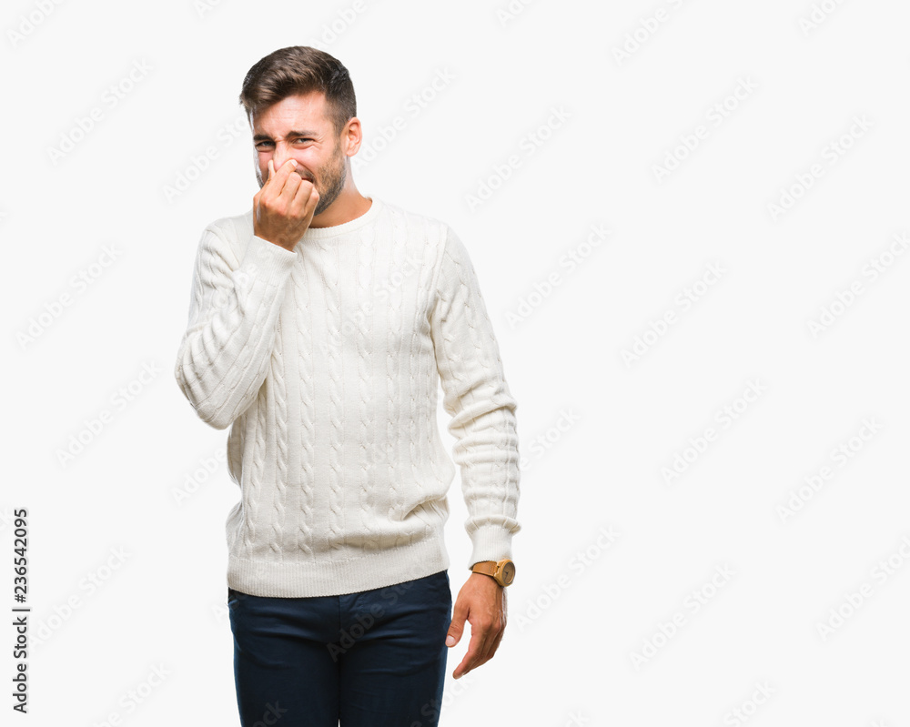 Young handsome man wearing winter sweater over isolated background smelling something stinky and disgusting, intolerable smell, holding breath with fingers on nose. Bad smells concept. Young handsome man wearing winter sweater over isolated background smelling something stinky and disgusting, intolerable smell, holding breath with fingers on nose. Bad smells concept.