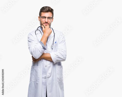 Young handsome doctor man over isolated background looking confident at the camera with smile with crossed arms and hand raised on chin. Thinking positive.