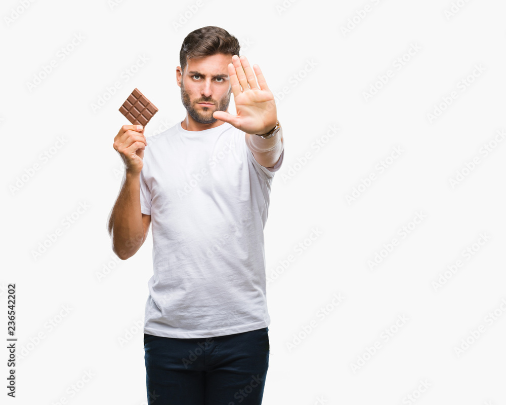 Young handsome man eating chocolate bar over isolated background with open hand doing stop sign with serious and confident expression, defense gesture Young handsome man eating chocolate bar over isolated background with open hand doing stop sign with serious and confident expression, defense gesture
