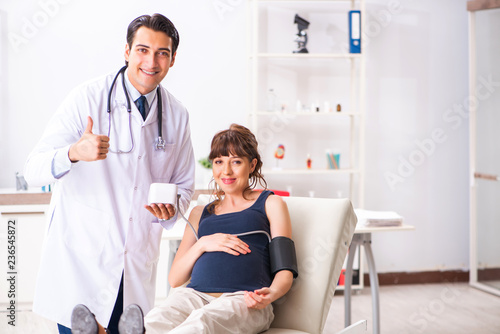 Young doctor checking pregnant woman s blood pressure