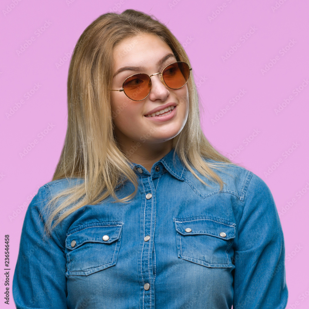 Young caucasian woman wearing sunglasses over isolated background looking away to side with smile on face, natural expression. Laughing confident. Young caucasian woman wearing sunglasses over isolated background looking away to side with smile on face, natural expression. Laughing confident.