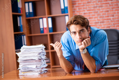 Young employee with excessive work sitting at the office  photo