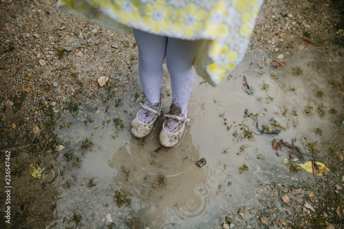 Little girls legs and feet as she jumps in muddy puddles while dressed up in satin, shoes and yellow dress. photo
