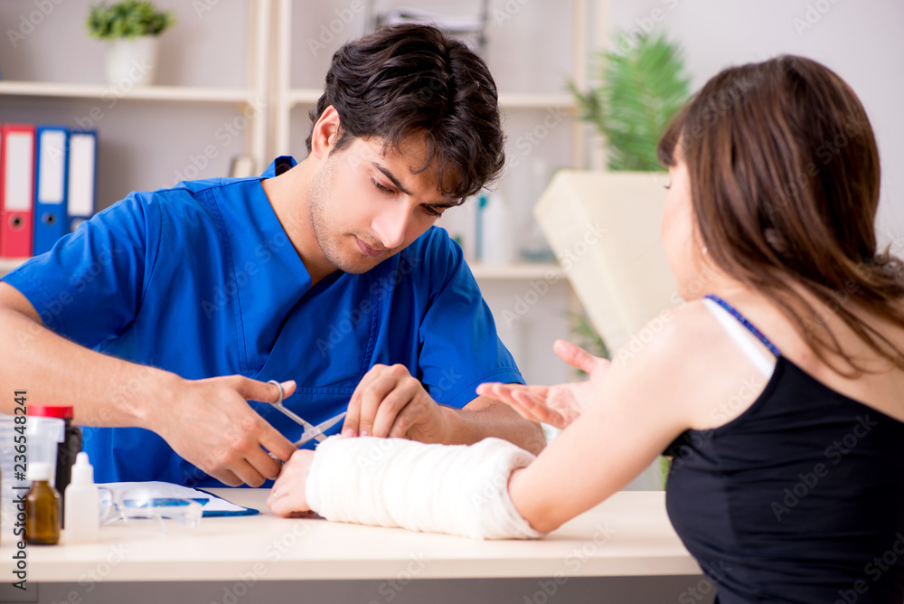 Young woman with bandaged arm visiting male doctor traumotologis Young woman with bandaged arm visiting male doctor traumotologis