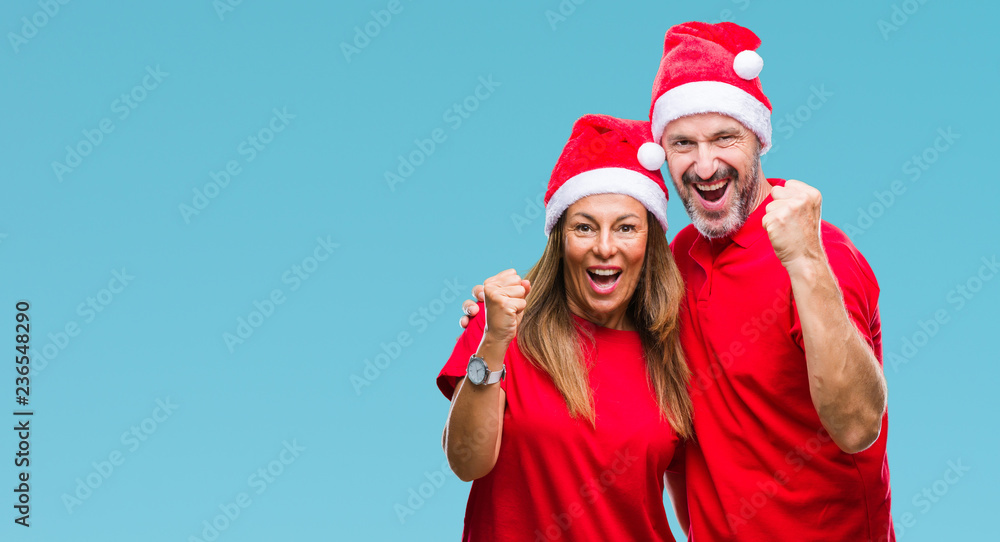 Middle age hispanic couple wearing christmas hat over isolated background celebrating surprised and amazed for success with arms raised and open eyes. Winner concept. Middle age hispanic couple wearing christmas hat over isolated background celebrating surprised and amazed for success with arms raised and open eyes. Winner concept.