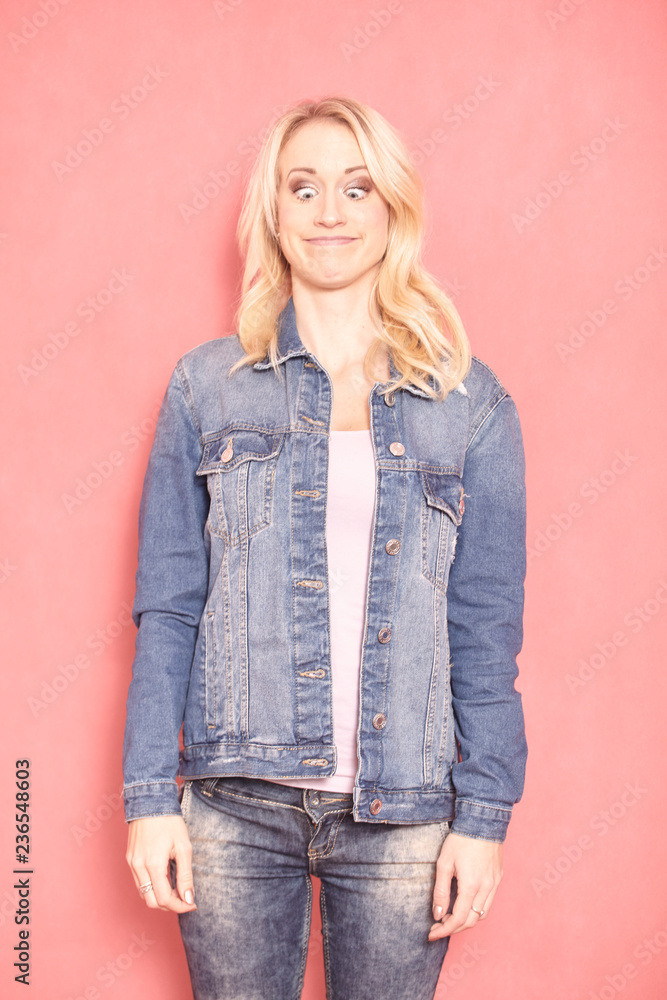one young woman, 20-29 years old, long blond hair. Shot in studio on pink background. looking down, eyes wide open, face expression acting like a frog, standing still (upper body shot). one young woman, 20-29 years old, long blond hair. Shot in studio on pink background. looking down, eyes wide open, face expression acting like a frog, standing still (upper body shot).