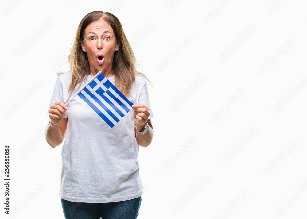 Middle age hispanic woman holding flag of Greece over isolated background scared in shock with a surprise face, afraid and excited with fear expression Middle age hispanic woman holding flag of Greece over isolated background scared in shock with a surprise face, afraid and excited with fear expression