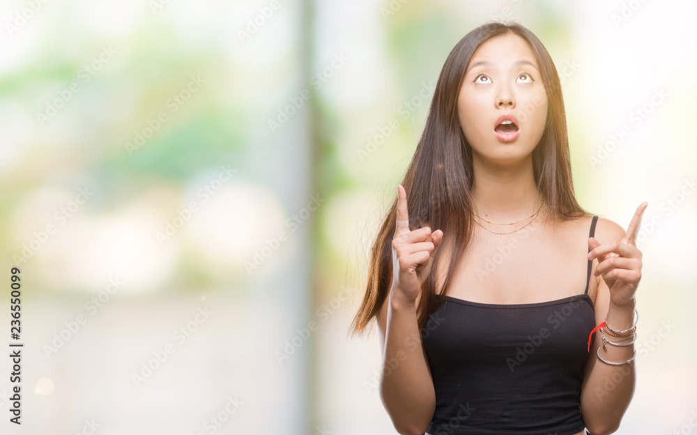 Young asian woman over isolated background amazed and surprised looking up and pointing with fingers and raised arms. Young asian woman over isolated background amazed and surprised looking up and pointing with fingers and raised arms.