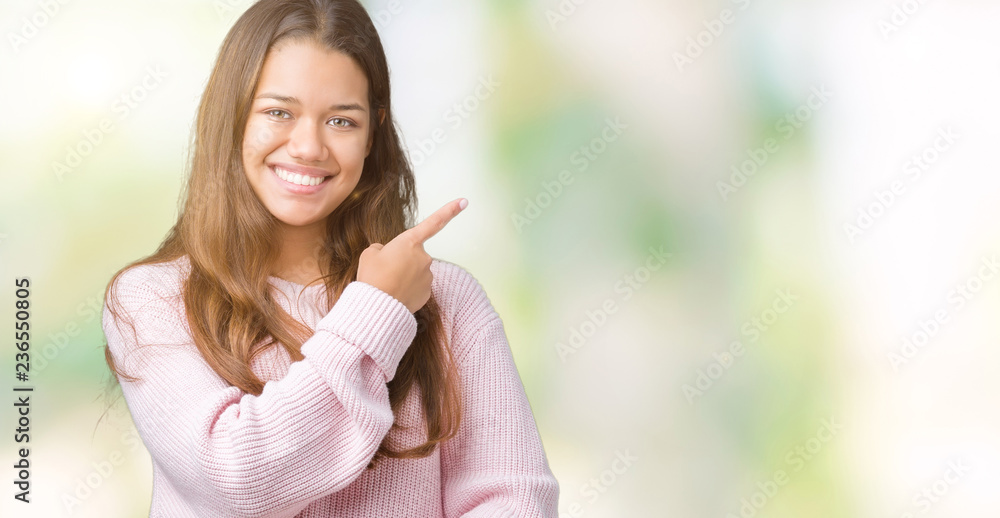 Young beautiful brunette woman wearing pink winter sweater over isolated background cheerful with a smile of face pointing with hand and finger up to the side with happy and natural expression on face Young beautiful brunette woman wearing pink winter sweater over isolated background cheerful with a smile of face pointing with hand and finger up to the side with happy and natural expression on face