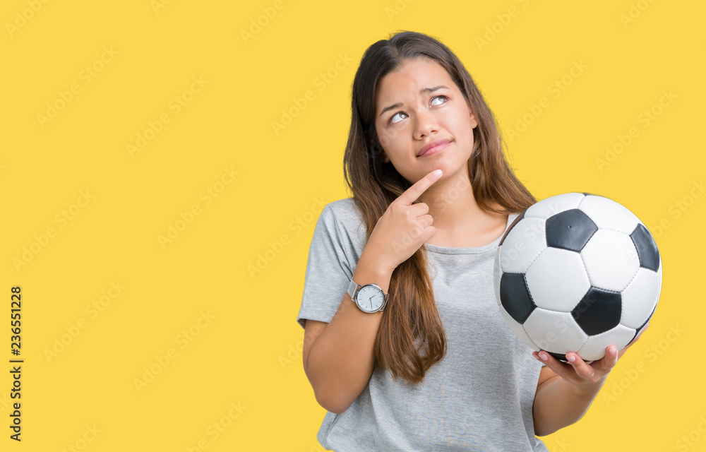 Young beautiful brunette woman holding soccer football ball over isolated background serious face thinking about question, very confused idea Young beautiful brunette woman holding soccer football ball over isolated background serious face thinking about question, very confused idea