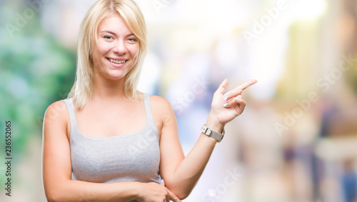 Young beautiful blonde woman over isolated background with a big smile on face, pointing with hand and finger to the side looking at the camera. © Krakenimages.com