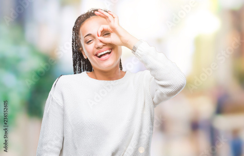 Young braided hair african american girl wearing winter sweater over isolated background doing ok gesture with hand smiling  eye looking through fingers with happy face.