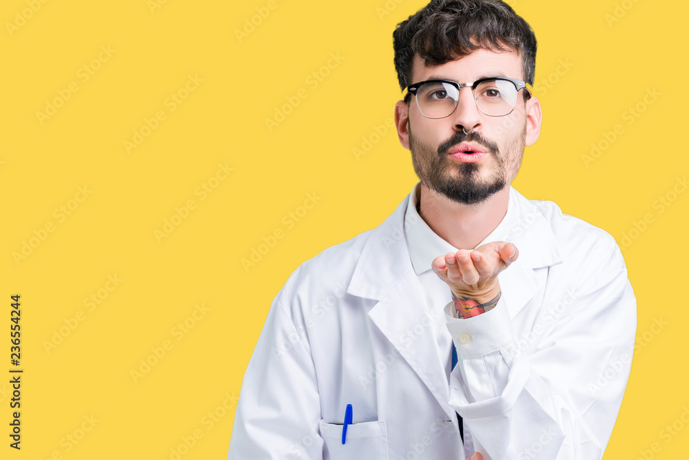 Young professional scientist man wearing white coat over isolated background looking at the camera blowing a kiss with hand on air being lovely and sexy. Love expression. Young professional scientist man wearing white coat over isolated background looking at the camera blowing a kiss with hand on air being lovely and sexy. Love expression.