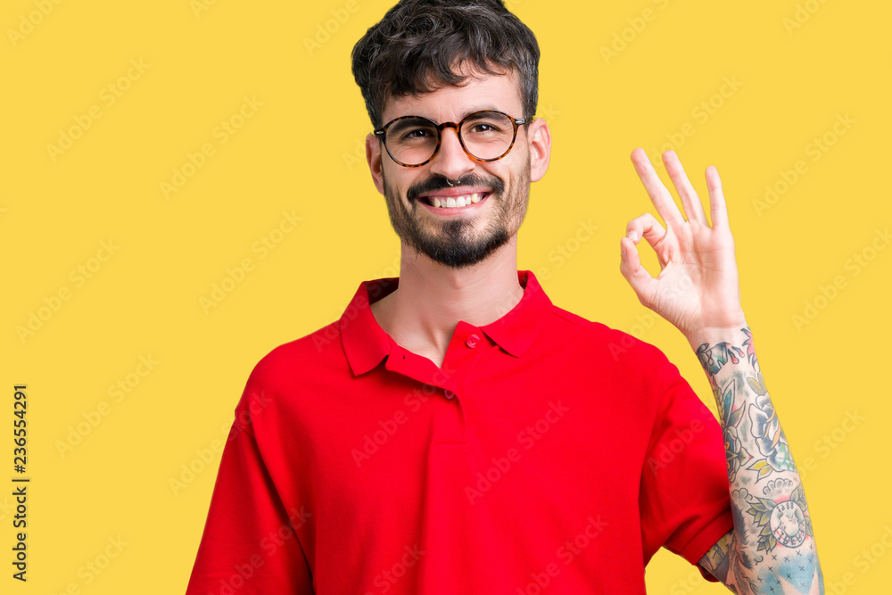 Young handsome man wearing glasses over isolated background smiling positive doing ok sign with hand and fingers. Successful expression. Young handsome man wearing glasses over isolated background smiling positive doing ok sign with hand and fingers. Successful expression.