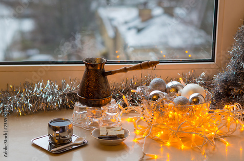 Christmas morning. Coffee in jezve, silver balls, garland and decorative tree on a window sill. Winter mood. Happy New Year