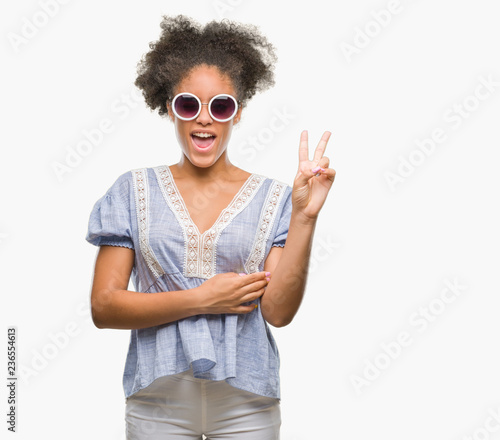 Young afro american woman wearing glasses over isolated background smiling with happy face winking at the camera doing victory sign. Number two.
