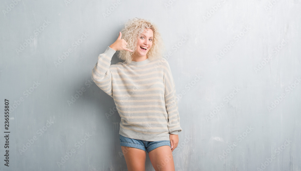 Young blonde woman with curly hair over grunge grey background smiling doing phone gesture with hand and fingers like talking on the telephone. Communicating concepts. Young blonde woman with curly hair over grunge grey background smiling doing phone gesture with hand and fingers like talking on the telephone. Communicating concepts.